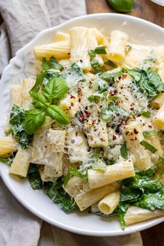 pasta with spinach, cheese and herbs in a white bowl on a wooden table