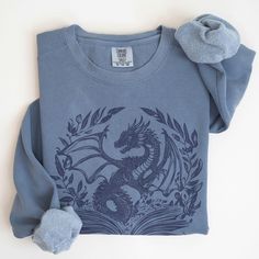 This cozy blue or green Comfort Colors® crewneck sweatshirt is the perfect matching book club merch, gift for a fantasy book lover, librarian or dragon girl, or outfit to bookworm up in for your latest dragon fantasy series!  80% ring-spun cotton and 20% polyester blend, 3-end garment-dyed, ring-spun, color-blast fleece with a 100% cotton face. Each sweatshirt comes with a relaxed fit, a rolled-forward shoulder, and a back neck patch.  .: 80% ring-spun cotton, 20% polyester .: Medium-heavy fabric (9.5 oz /yd² (322.1 g/m .: Relaxed fit .: Sewn in twill label .: OEKO-TEX certified low-impact dyes Because these shirts are printed to order we can't accept returns or exchanges, however if something isn't right please contact us and we'll absolutely help make it right!  Thank you for shopping sm Bookish Shirts, Dragon Sweater, Club Merch, Dragon Book, Gift For Book Lover, Dragon Girl, Club Sweatshirts, Fantasy Book, Book Dragon