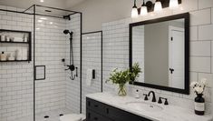 a bathroom with black and white tile walls, a large mirror over the sink, and a walk in shower