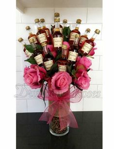 a vase filled with lots of pink flowers and bottles of liquor sitting on top of a counter