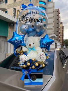 a white teddy bear sitting in the back of a car with blue and silver balloons