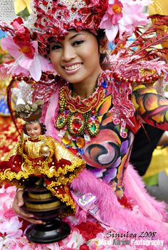 a woman dressed in pink and gold holding a vase with a doll on top of it