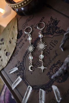 * Stunning, yet dainty! These mismatched Moon and Stars earrings which will give your outfit a mystical touch. One features a little star, while the other one has a Moon. You can choose several different colors! * These beautiful dangling earrings have a witchy, bohemian, whimsigoth feel to them, and are decorated with charms and sparkly glass beads. * Stainless steel! * The total length of the earrings is approximately 7 cm (aprox 3 inches), hook included.  * They come in a pretty little burlap pouch 🖤 *Matching necklace available here: https://www.etsy.com/listing/1565444762/personalizable-silver-moon-or-star Celestial Silver Pierced Crystal Earrings, Silver Celestial Crystal Earrings For Pierced Ears, Celestial Star Cartilage Earring, Silver Celestial Crystal Earrings, Silver Celestial Crystal Earrings With Moon Charm, Celestial Silver Crystal Earrings With Moon Charm, Silver Celestial Crystal Earrings Nickel Free, Whimsigoth Jewelry, Boho Whimsigoth