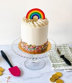 a white cake with sprinkles and a rainbow decoration on top sits on a table