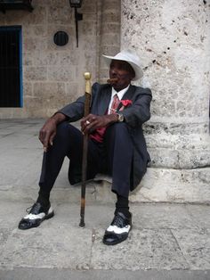 a man in a suit and hat sitting on the ground with a cane next to him