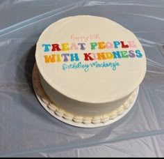 there is a white cake with rainbow lettering on it that says treat people with kindness