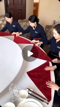 three women in uniforms are cutting up a red and white tablecloth on a couch