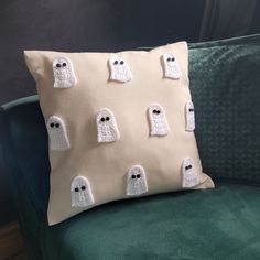 a pillow with crocheted ghost faces on it sitting on a green chair in front of a window