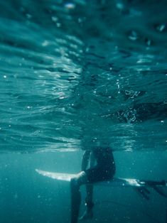 a person sitting on a surfboard under the water's surface, with their back to the camera