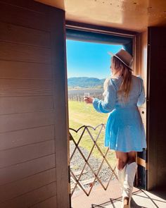 a woman in a blue dress and cowboy hat looking out the window