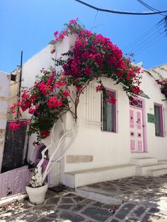 a white house with pink flowers growing on it's side and stairs leading up to the door