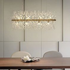 a chandelier hanging over a wooden table with white chairs and a vase on it