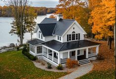 an aerial view of a white house with black roofing and trees in the background