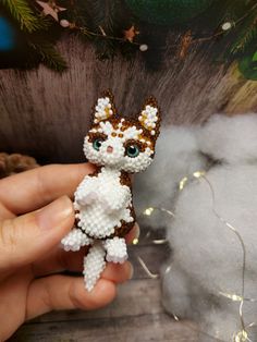 someone is holding a tiny cat made out of bead and yarn with lights in the background