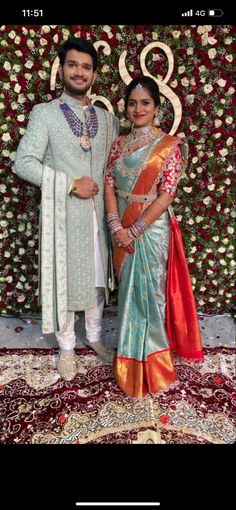 two people standing next to each other in front of a flower wall