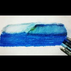 two crayons are next to a drawing of a blue ocean wave with a surfer on it