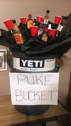 a bucket filled with lots of liquor bottles sitting on top of a wooden table next to a sign that says puke bucket