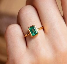 a woman's hand with a gold ring and an emerald stone on the finger