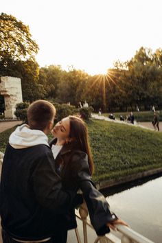 a man and woman standing next to each other in front of a lake at sunset