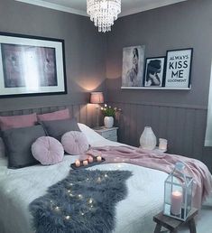 a bedroom decorated in shades of grey and pink with candles on the bed, framed pictures above