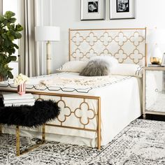 a white and gold bedroom with two pictures on the wall above the bed, along with an ottoman