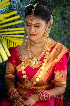 a woman in a red and gold sari sitting down with her hands on her chest