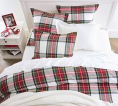 a bed with plaid sheets and pillows on top of it next to a night stand