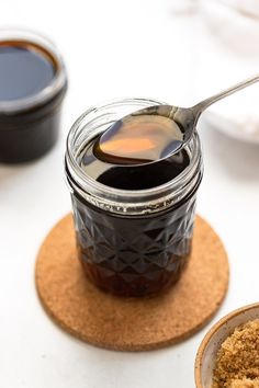 a spoon full of honey sitting on top of a coaster next to some sauce in a jar