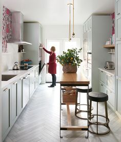 a woman standing in a kitchen next to a table with a potted plant on it