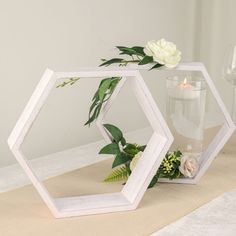 two white hexagonal mirrors sitting on top of a table next to a vase filled with flowers