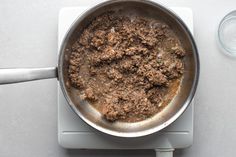 a frying pan filled with food on top of a white surface next to a glass of water