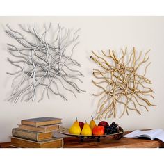 two metal wall art pieces with fruit and books on a table next to each other