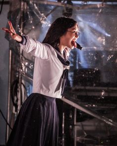 a woman singing into a microphone while standing in front of a stage with her arms outstretched