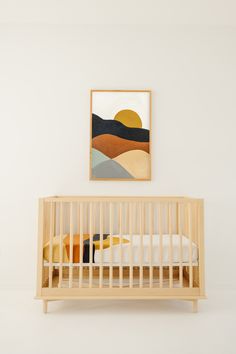 a baby crib in a white room with a painting on the wall above it