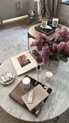 a table topped with books and flowers on top of a white coffee table next to a window