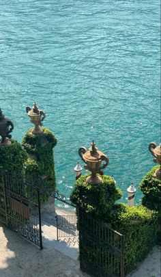 an iron fence with potted plants on top next to the water's edge