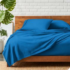 a bed with blue sheets and pillows on top of it next to a potted plant