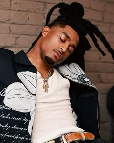 a man with dreadlocks laying on his back in front of a brick wall