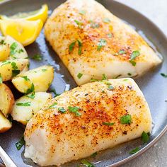 two fish fillets on a plate with potatoes and lemon wedges