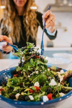 a woman is cutting into a salad with blue utensils