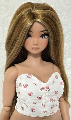 a doll is wearing a white top with pink flowers on it's chest and long blonde hair