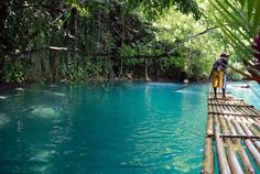 a man is standing on a bamboo bridge over the blue water that runs through the jungle