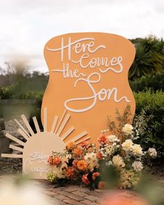 there is a sign that says here comes the son with flowers in front of it