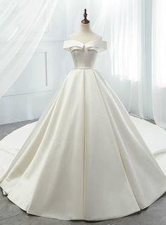 a white wedding dress on a mannequin in front of a window with curtains