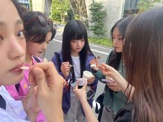 several girls are standing on the street and eating food from small containers in front of them