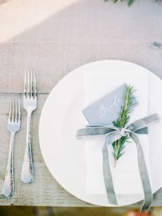 a place setting with napkins, silverware and greenery tied around the edge