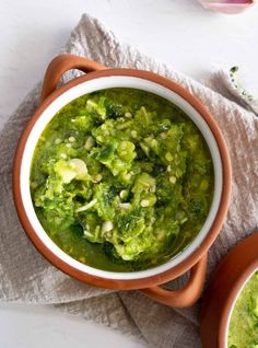 two bowls filled with broccoli soup on top of a cloth next to some spoons