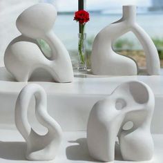 three white sculptures sitting on top of a table next to a vase with a flower in it