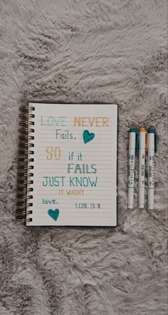 two pens are sitting next to a notebook with the words love never written on it