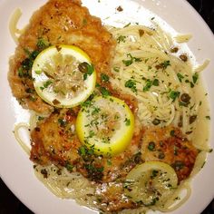 a white plate topped with pasta and meat covered in lemon slices, sauce and parmesan cheese